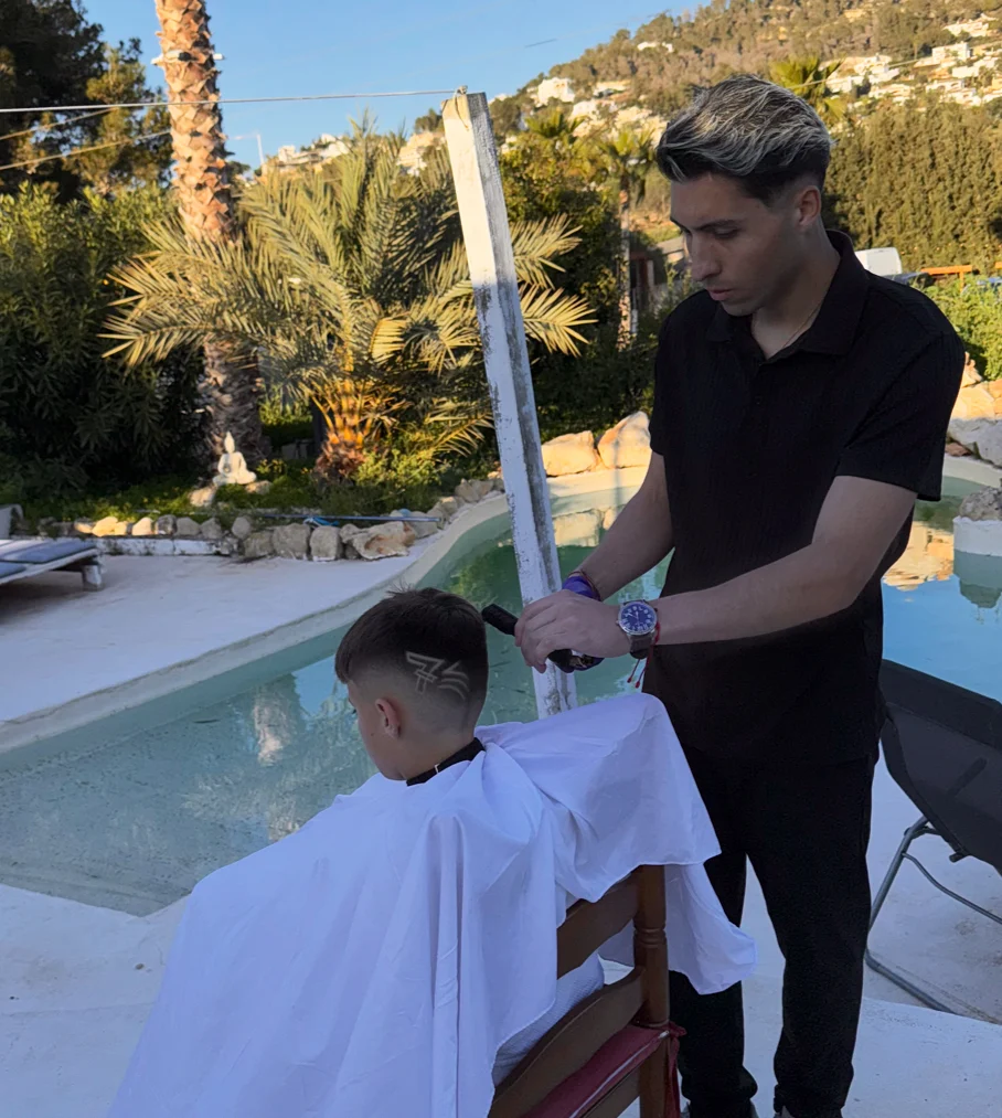 Ali cortando el pelo a un niño junto a la piscina de una villa